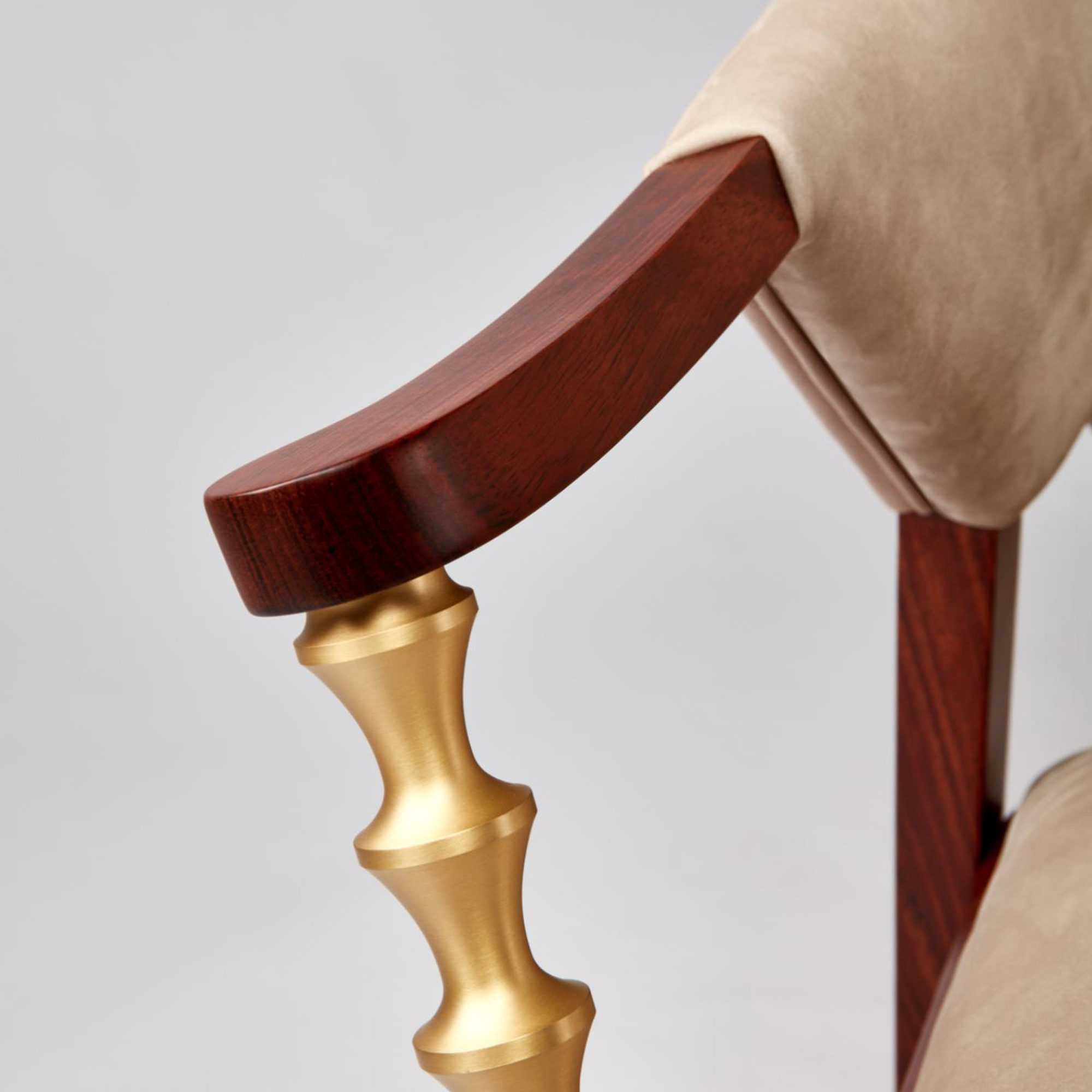 A detailed close-up showcasing the artistic brushed brass arm support with its sculptural hourglass segments, the rich mahogany wood armrest, and the premium beige nubuck leather upholstery, highlighting the exceptional craftsmanship and material quality.